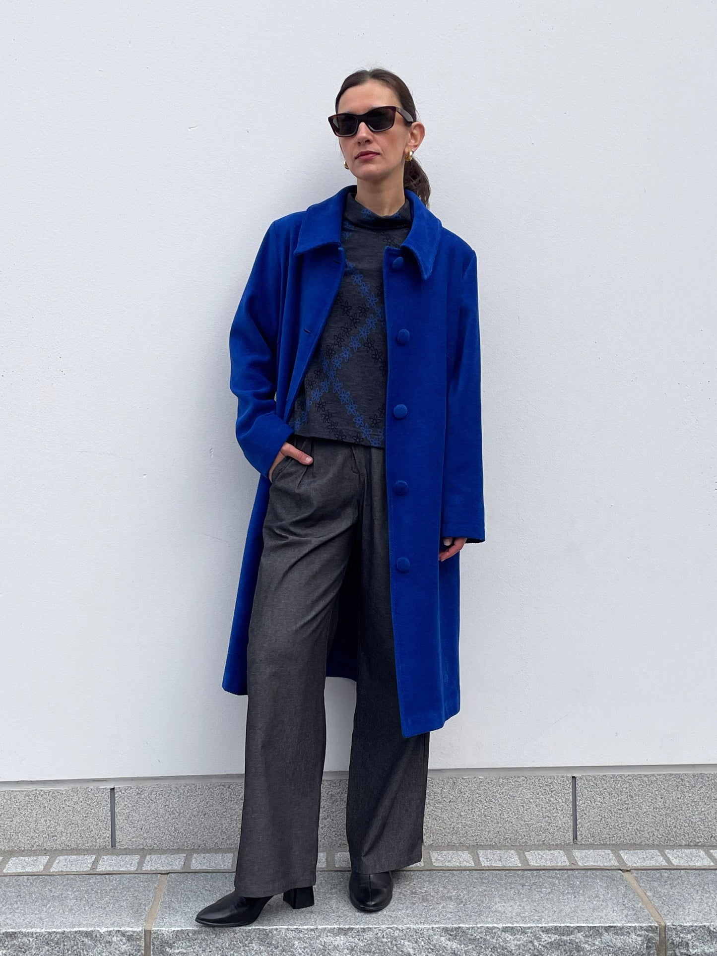 Person wearing a blue coat and gray pants against a white wall.